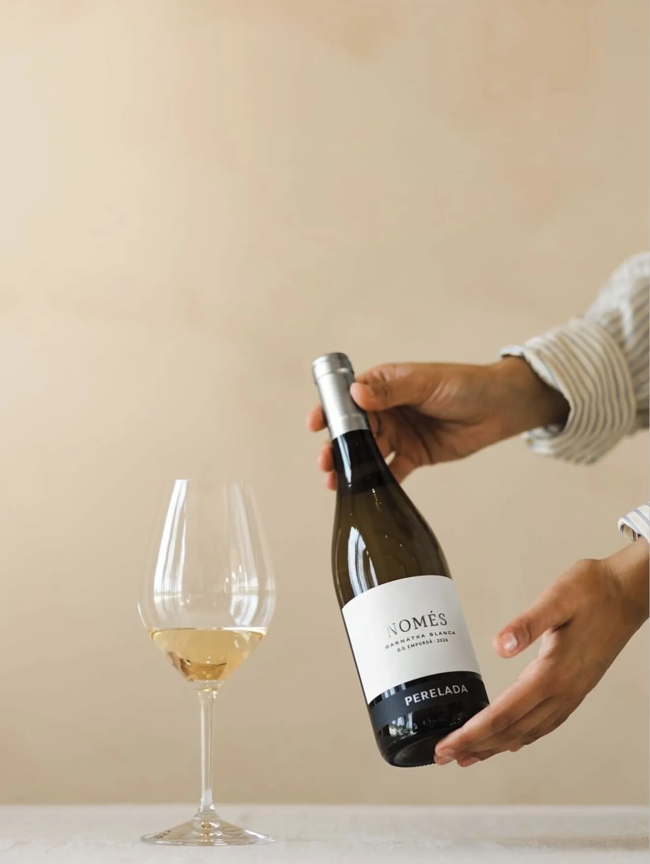 Sirviendo una botella de Perelada Només junto a una copa de vino blanco